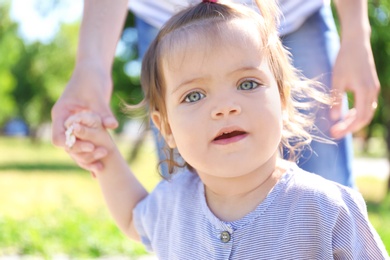 Adorable baby girl holding mother's hand while learning to walk outdoors