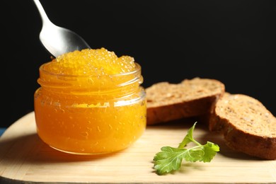 Fresh pike caviar in glass jar, bread and parsley on wooden board, closeup