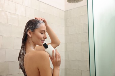 Photo of Young woman with bottle of shampoo in shower at home, space for text. Washing hair