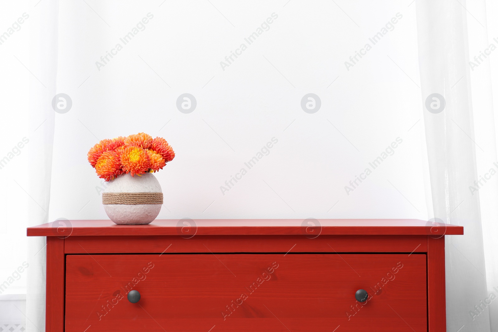 Photo of Red wooden chest of drawers with fresh flowers near white wall indoors