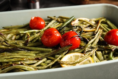 Delicious baked green beans with lemon and tomatoes in dishware, closeup