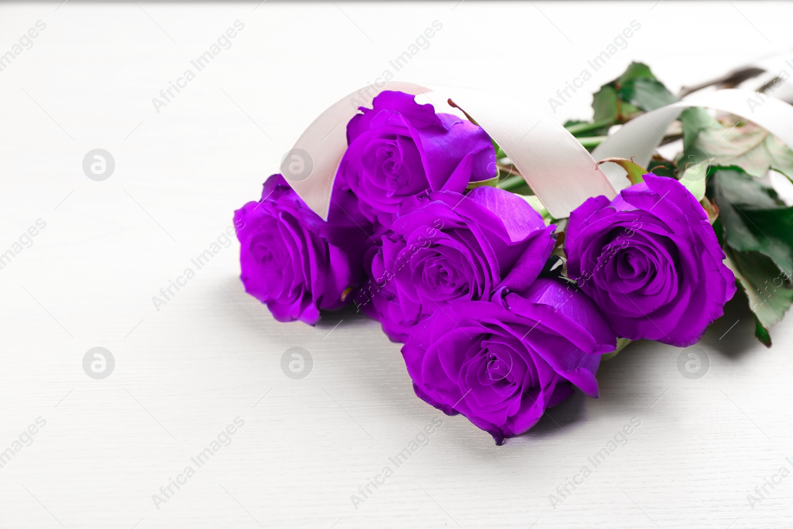 Image of Violet roses on white wooden table, space for text. Funeral attributes