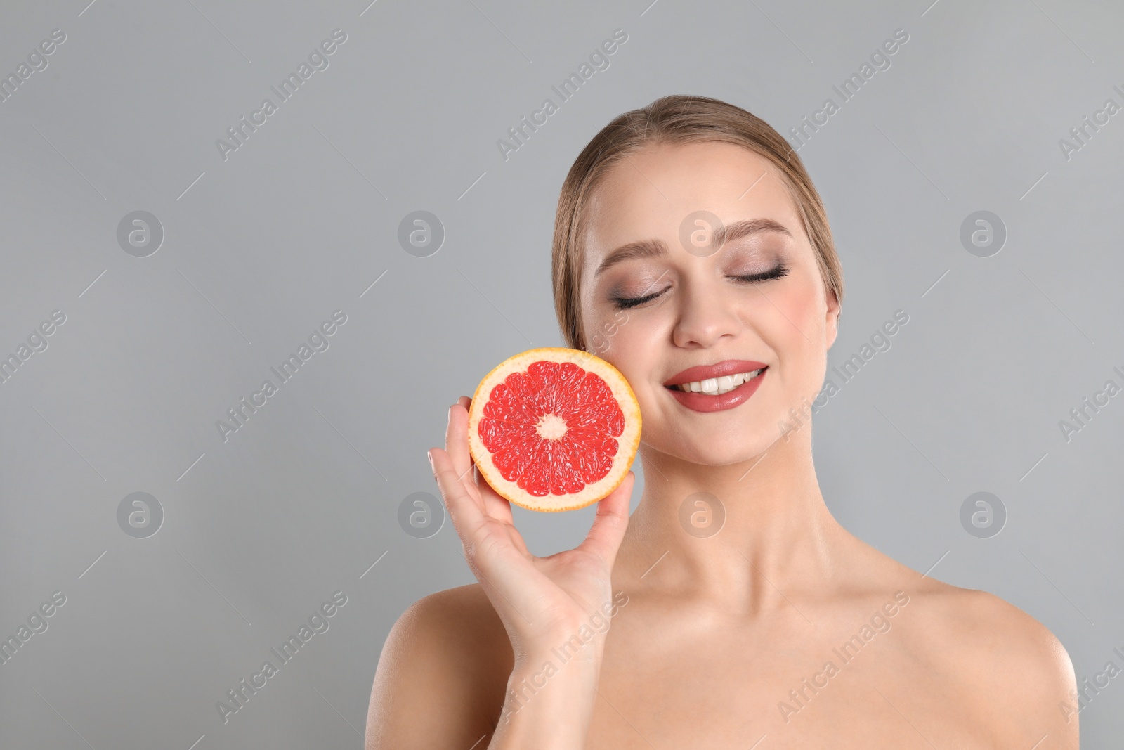 Photo of Young woman with cut grapefruit on grey background, space for text. Vitamin rich food