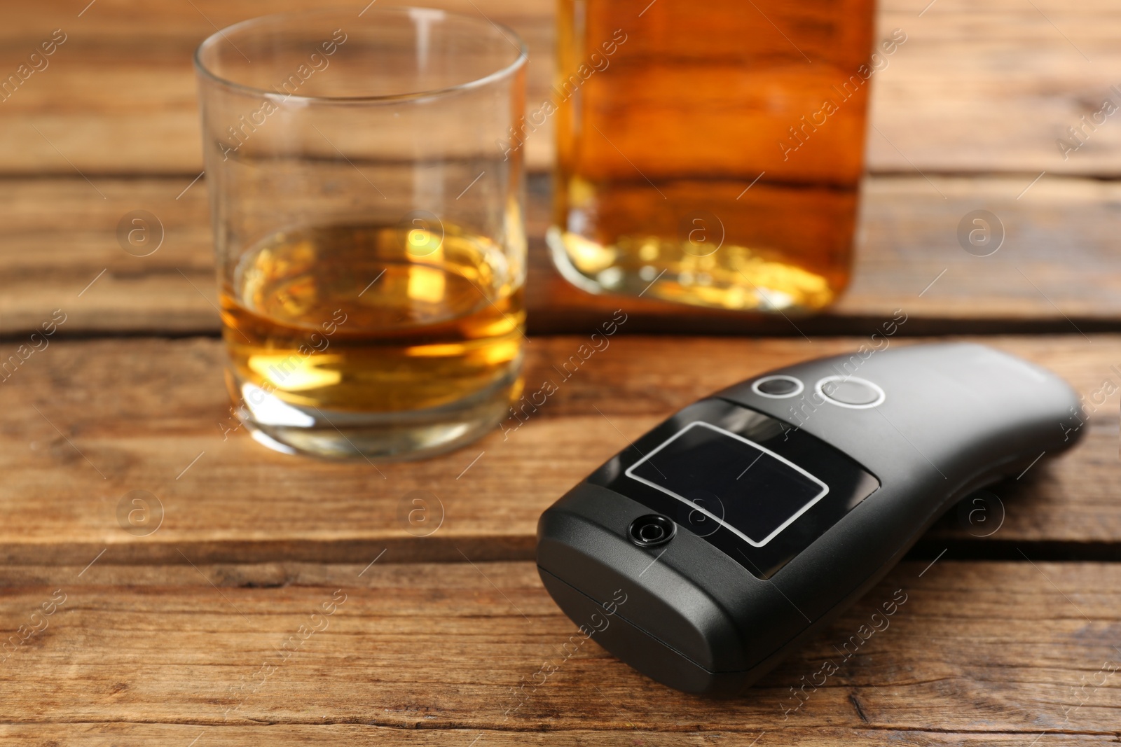Photo of Modern breathalyzer and alcohol on wooden table