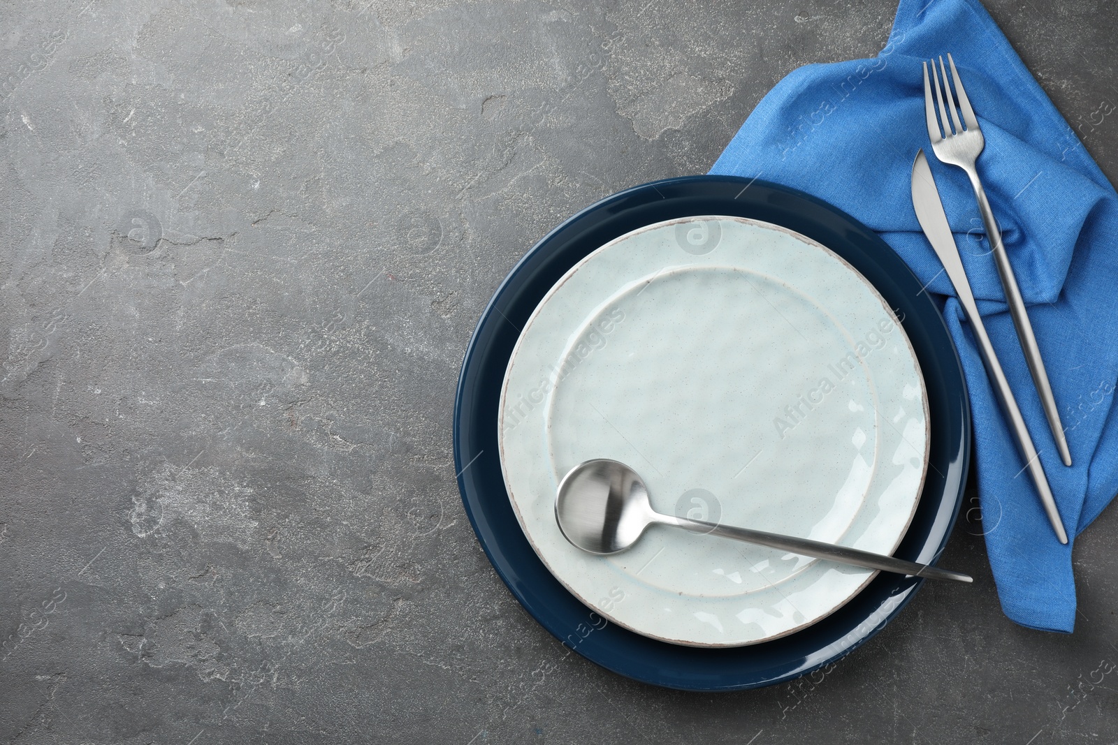 Photo of Stylish setting with cutlery, plates and napkin on grey textured table, flat lay. Space for text