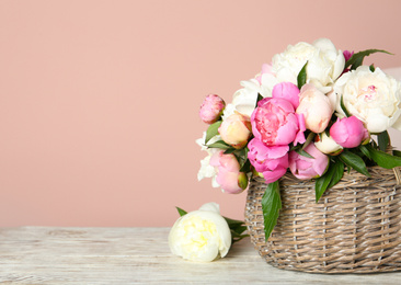 Photo of Basket with beautiful peonies on wooden table. Space for text