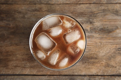 Glass of coffee with ice cubes on wooden background, top view