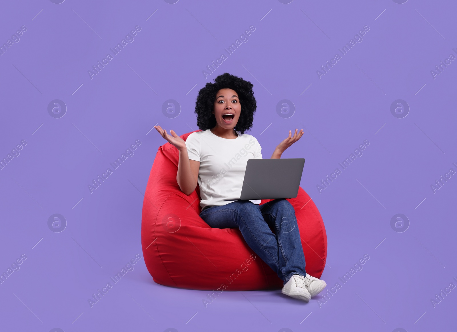 Photo of Emotional young woman with laptop sitting on beanbag chair against purple background