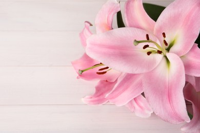 Photo of Beautiful pink lily flowers on white wooden table, closeup. Space for text