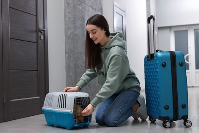 Photo of Travelling with pet. Smiling woman looking at carrier with her dog in hall