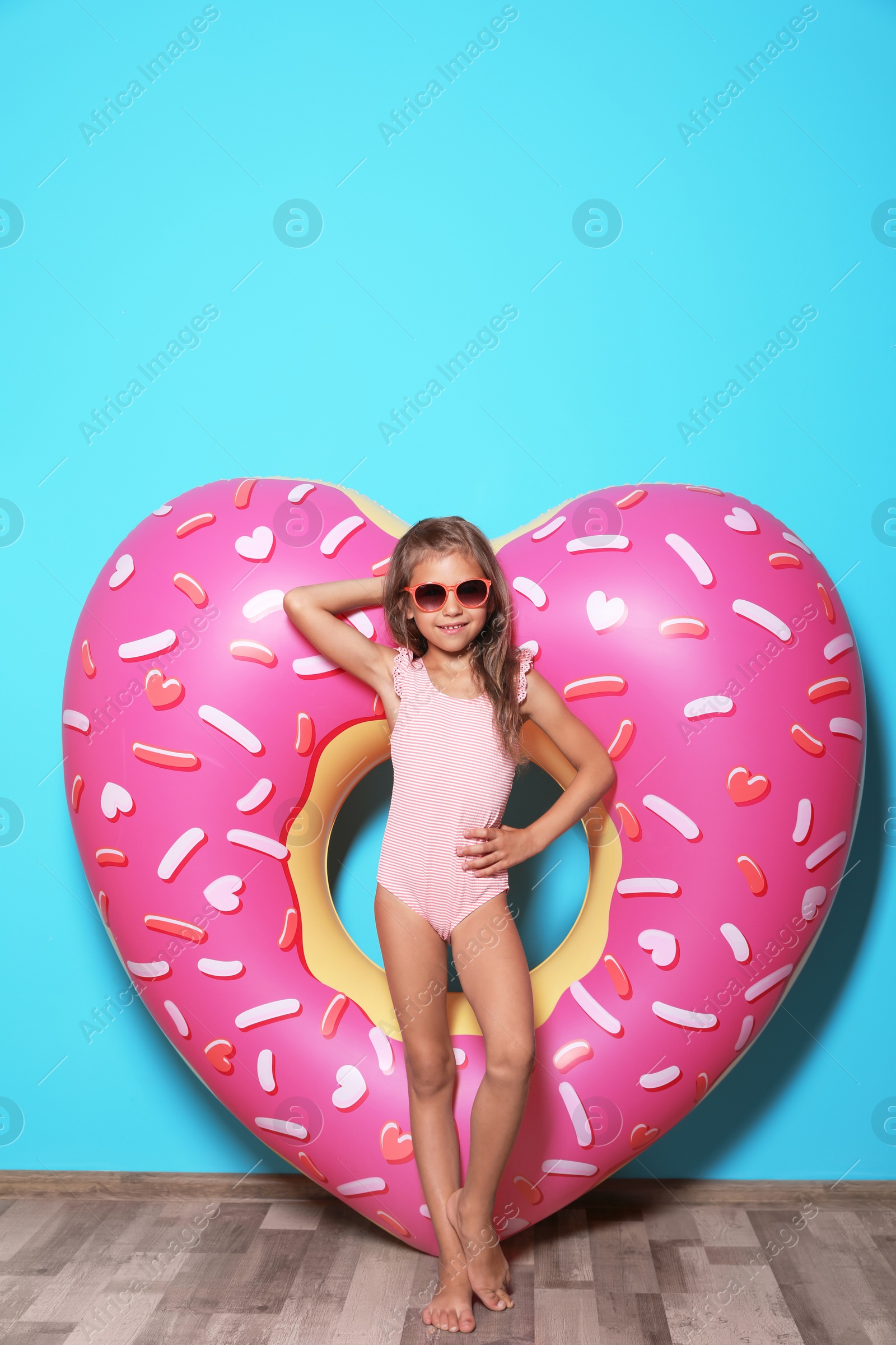 Photo of Cute little girl with bright heart shaped inflatable ring near color wall