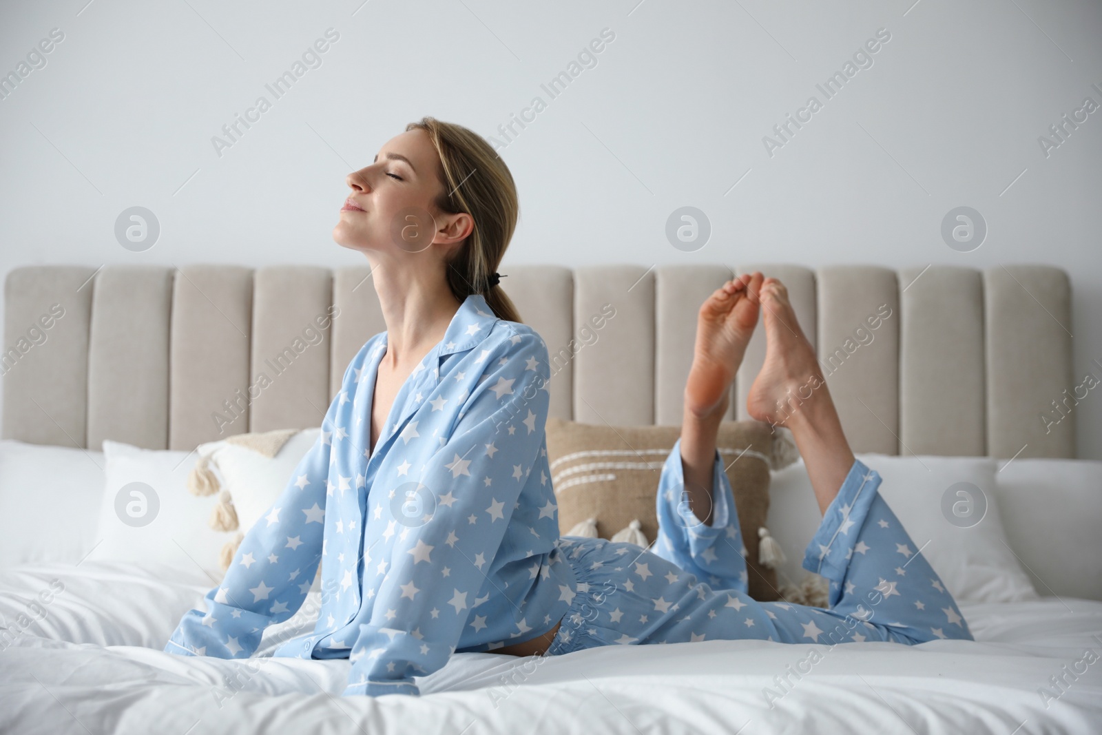 Photo of Young woman doing gymnastics on bed at home. Morning fitness