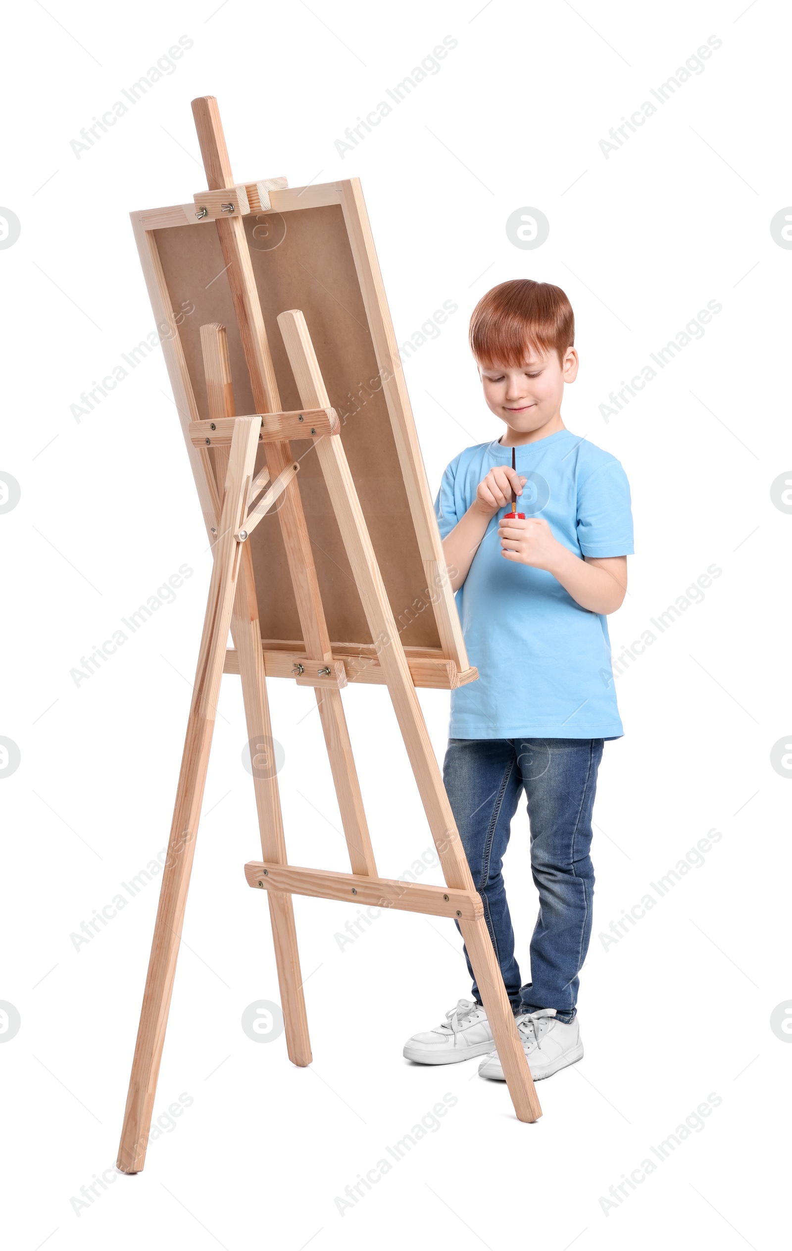 Photo of Little boy painting against white background. Using easel to hold canvas