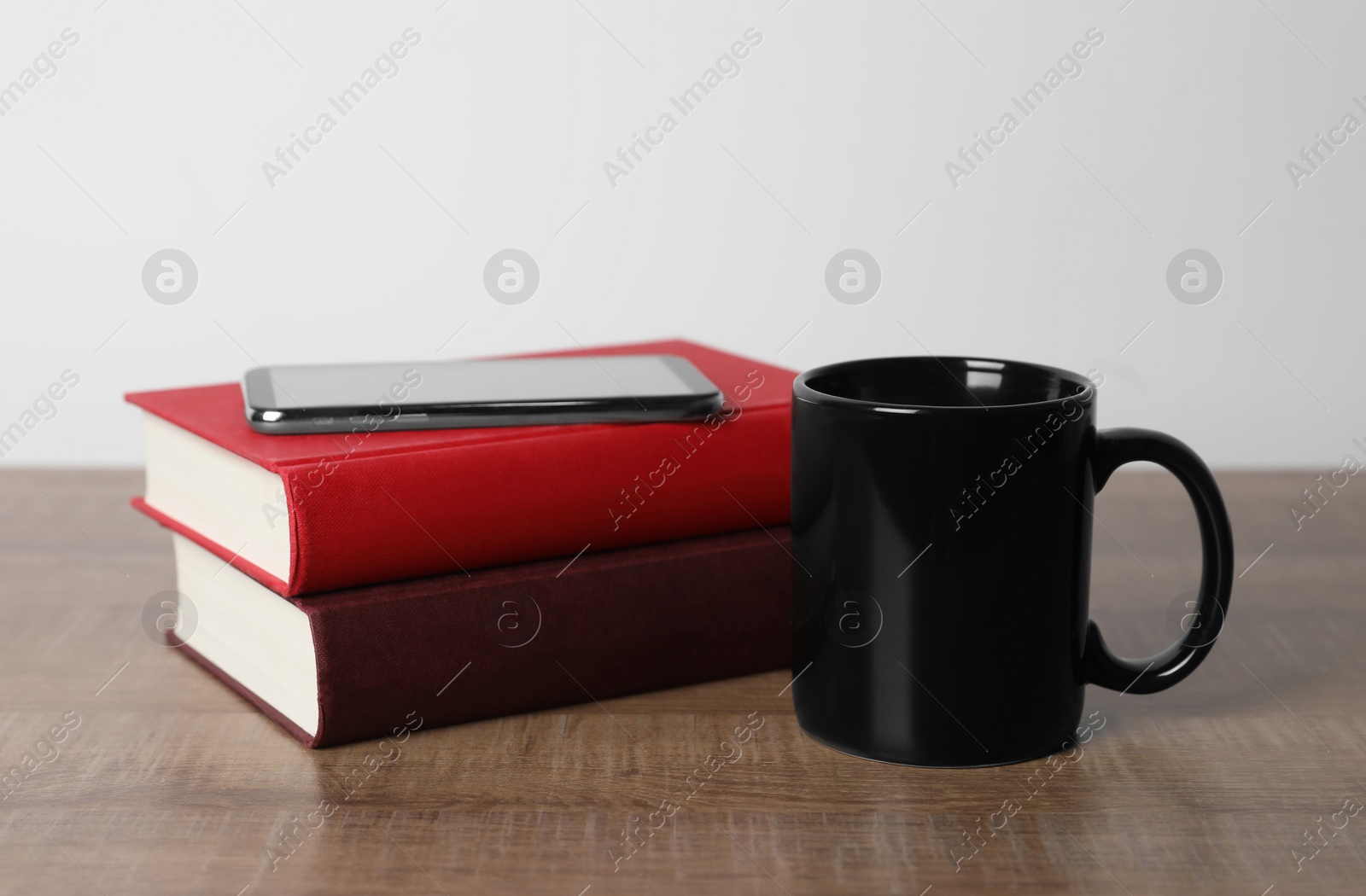 Black ceramic mug, stack of books and smartphone on wooden table Photo of Black ceramic mug, stack of books and smartphone on wooden table