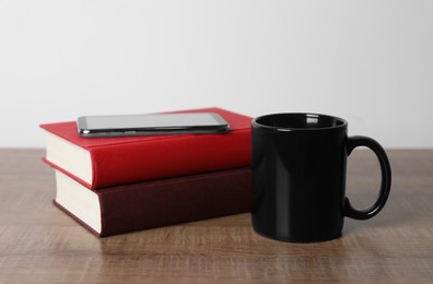 Photo of Black ceramic mug, stack of books and smartphone on wooden table