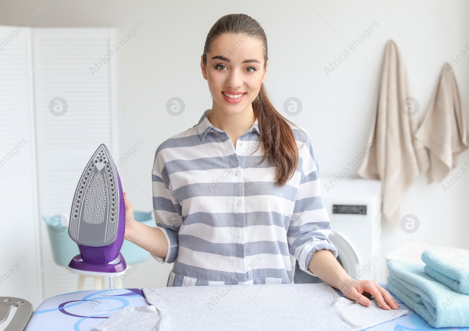 Photo of Young woman ironing clothes at home