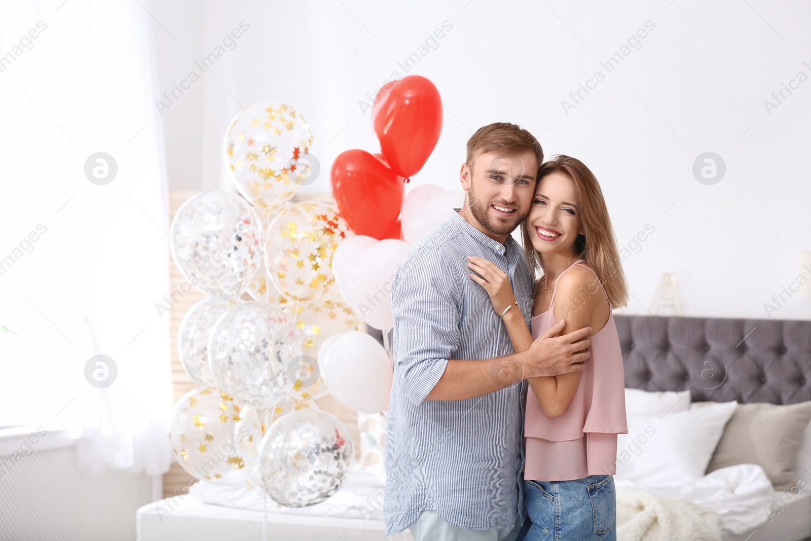 Photo of Young couple with air balloons in bedroom. Celebration of Saint Valentine's Day