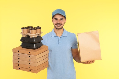 Young courier with different orders on color background. Food delivery service