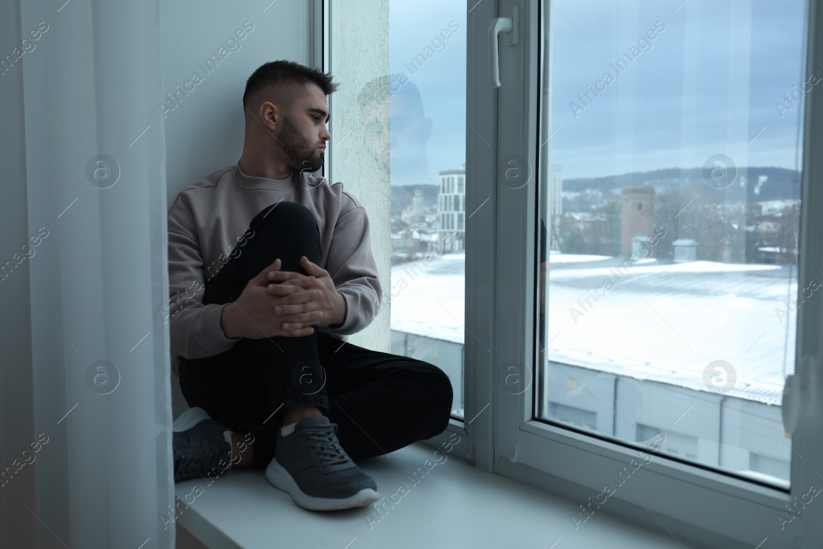 Photo of Sad man sitting on sill and looking at window indoors