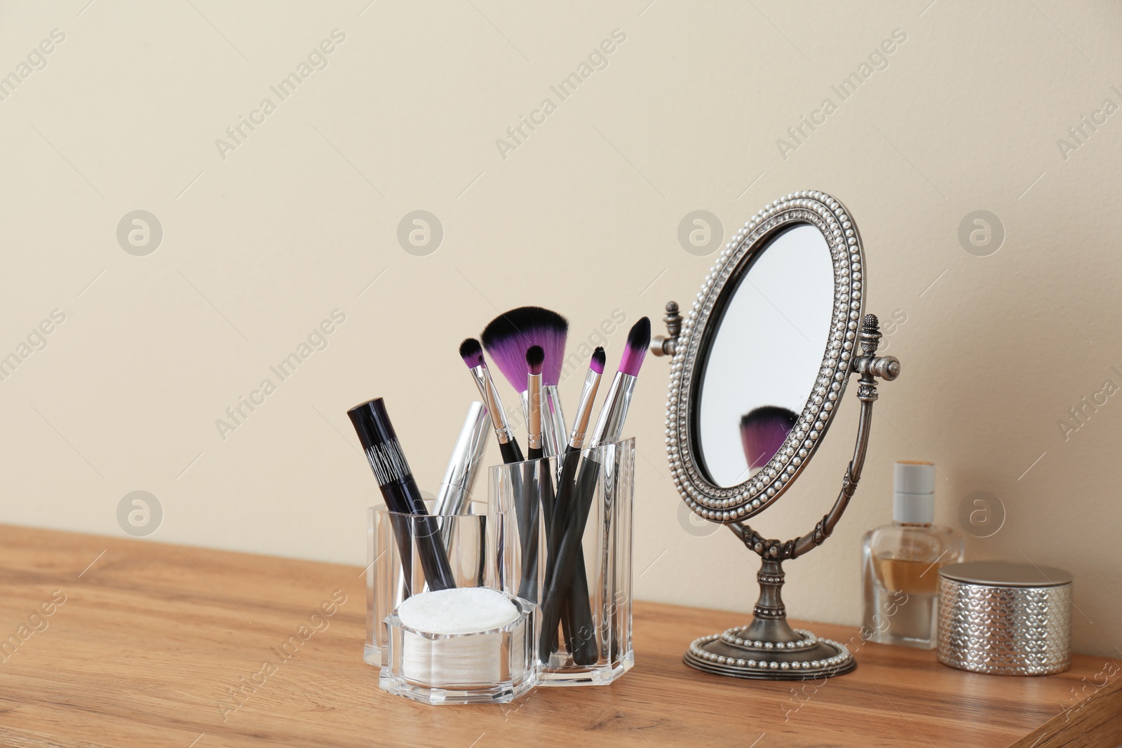 Photo of Organizer with cosmetic products for makeup and mirror on table against light wall