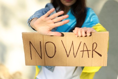 Young woman holding poster with words No War and showing stop gesture near light wall, closeup