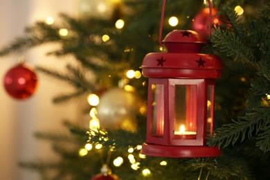Photo of Christmas lantern with burning candle on fir tree against blurred background, closeup. Space for text
