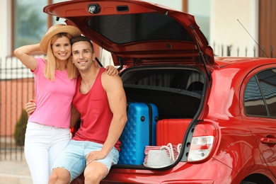 Happy couple near car trunk with suitcases outdoors