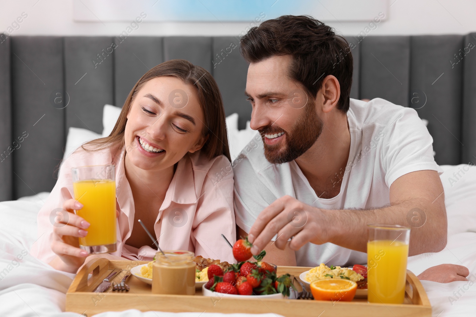 Photo of Happy couple eating tasty breakfast on bed at home