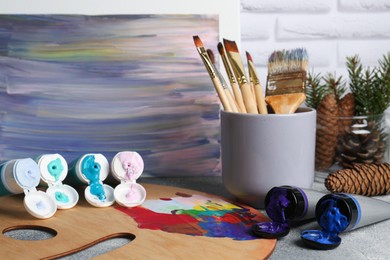 Photo of Artist's palette, tubes of colorful paints and brushes on textured table