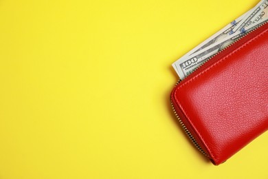 Stylish red leather purse with dollar banknotes on yellow background, top view. Space for text