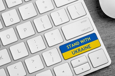 Image of Button in colors of Ukrainian flag with phrase Stand With Ukraine on keyboard, closeup view