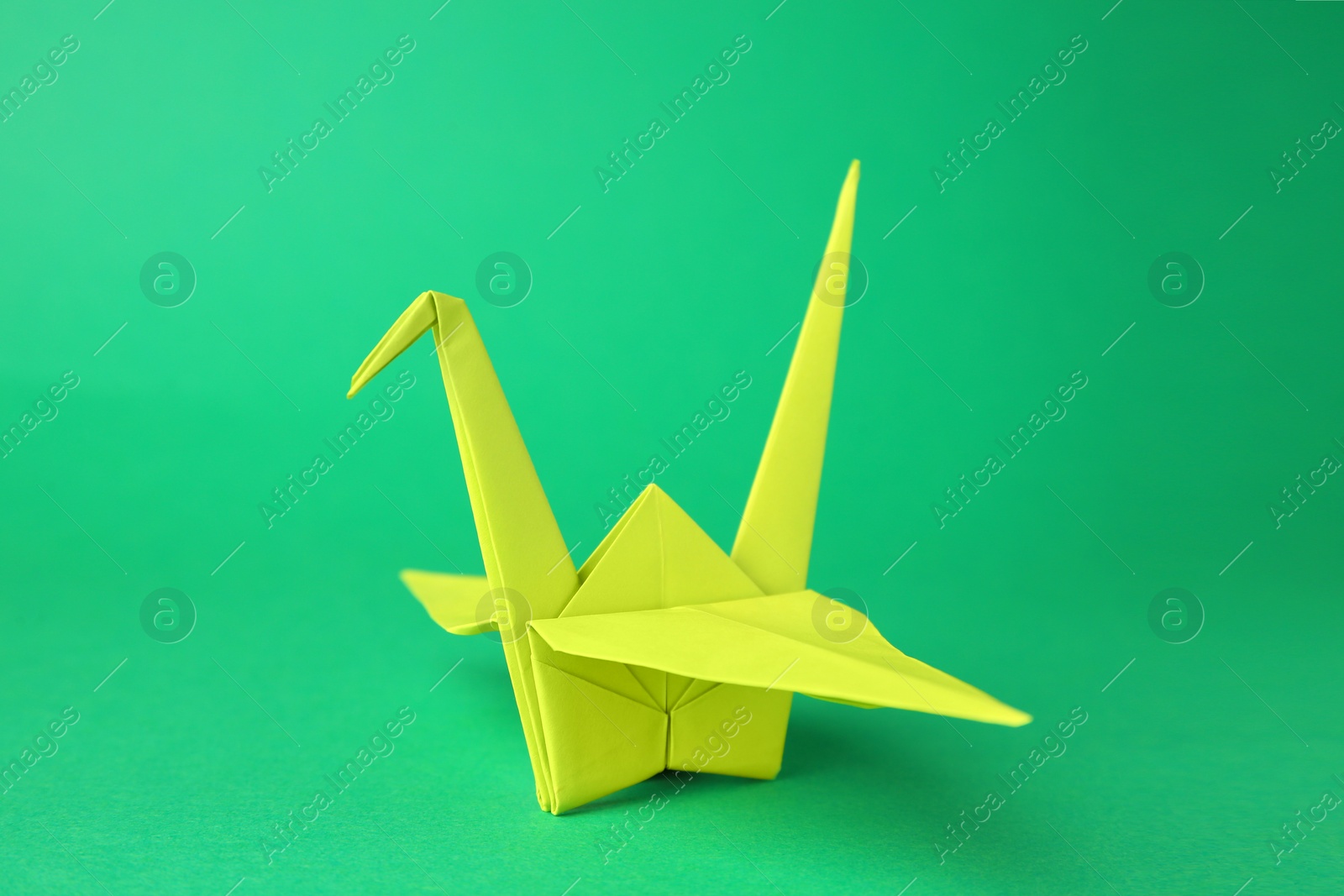 Photo of Paper origami crane on green background, closeup