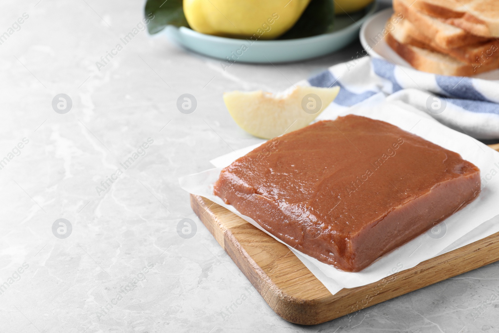 Photo of Wooden board with fresh quince paste on light grey marble table, space for text