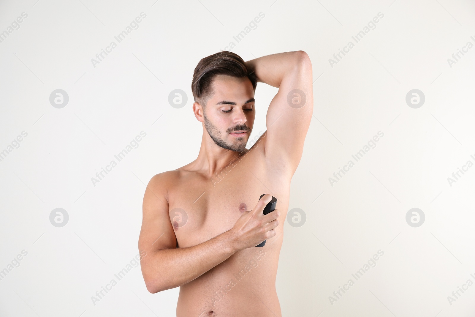 Photo of Young man using deodorant on white background