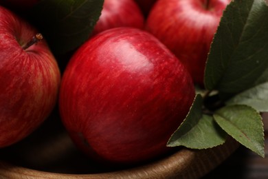 Photo of Ripe red apples and green leaves in wooden bowl on table, closeup