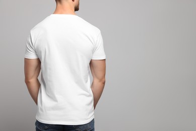 Man wearing white t-shirt on light grey background, back view. Mockup for design