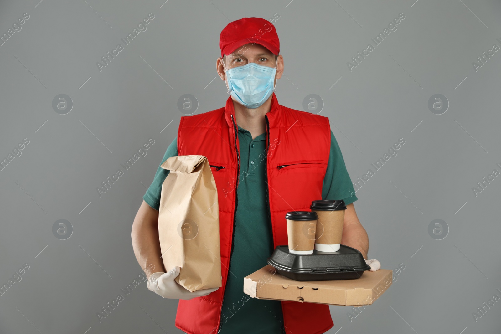 Photo of Courier in protective mask and gloves holding order on light grey background. Food delivery service during coronavirus quarantine