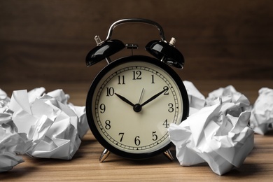 Crumpled paper balls and alarm clock on wooden table