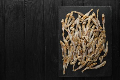 Photo of Delicious dried anchovies on black wooden table, top view. Space for text