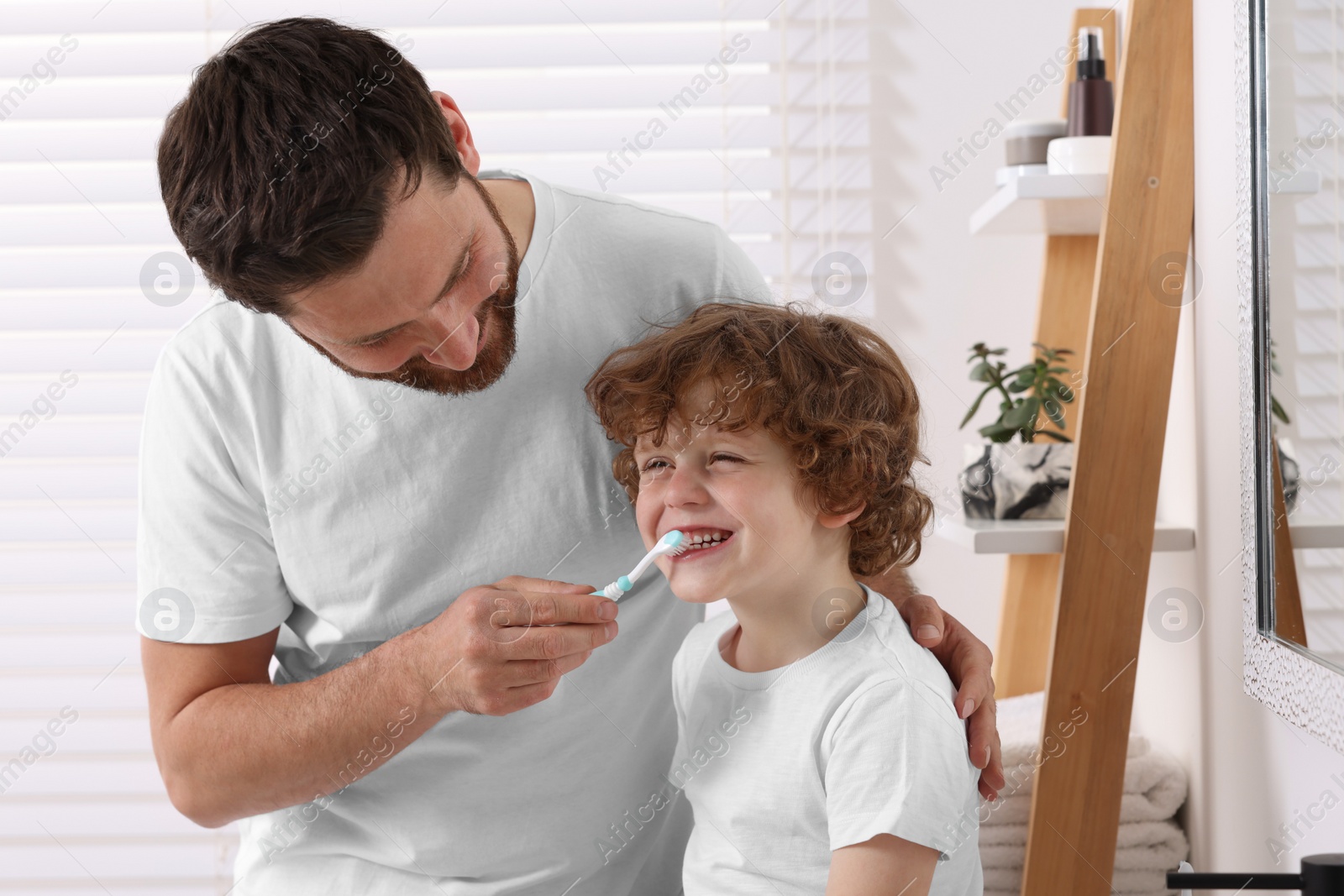 Photo of Father helping his son to brush teeth in bathroom