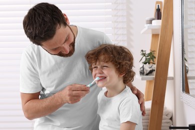 Father helping his son to brush teeth in bathroom