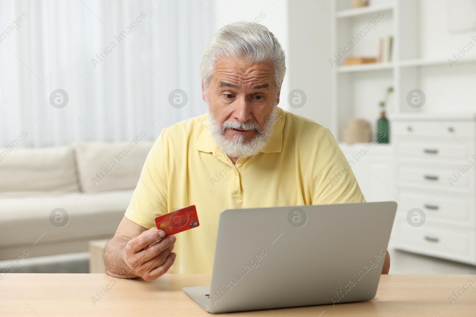 Photo of Stressful senior man with credit card using laptop at home. Be careful - fraud