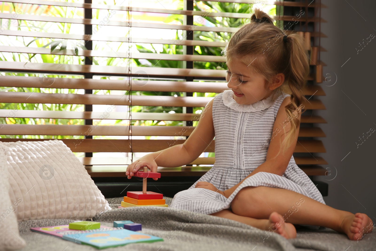 Photo of Cute little girl playing near window at home