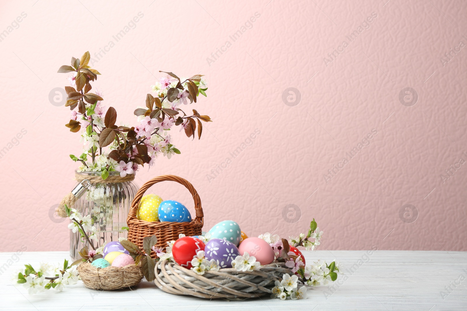 Photo of Composition with painted Easter eggs and blossoming branches on table. Space for text