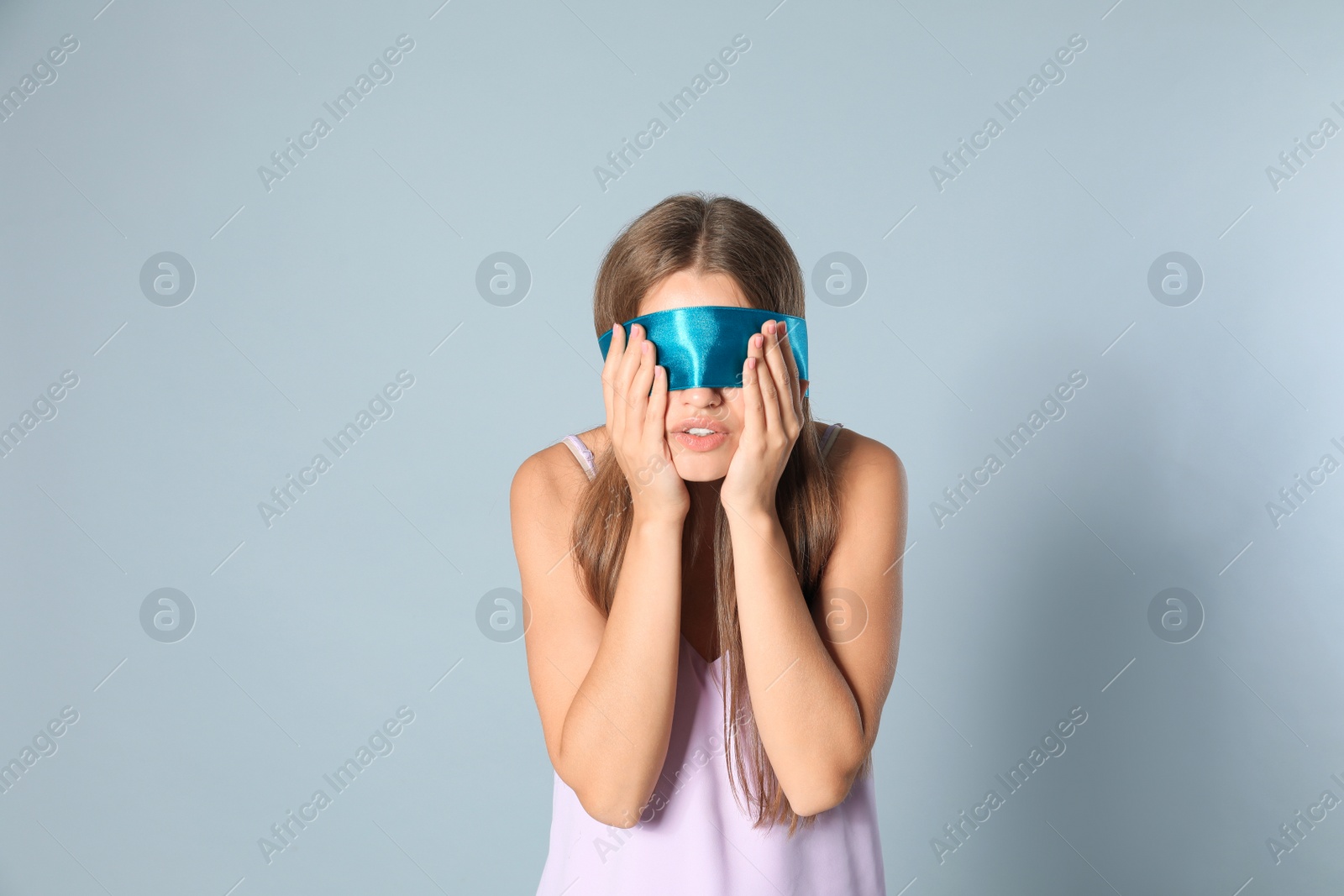 Photo of Young woman with light blue blindfold on grey background