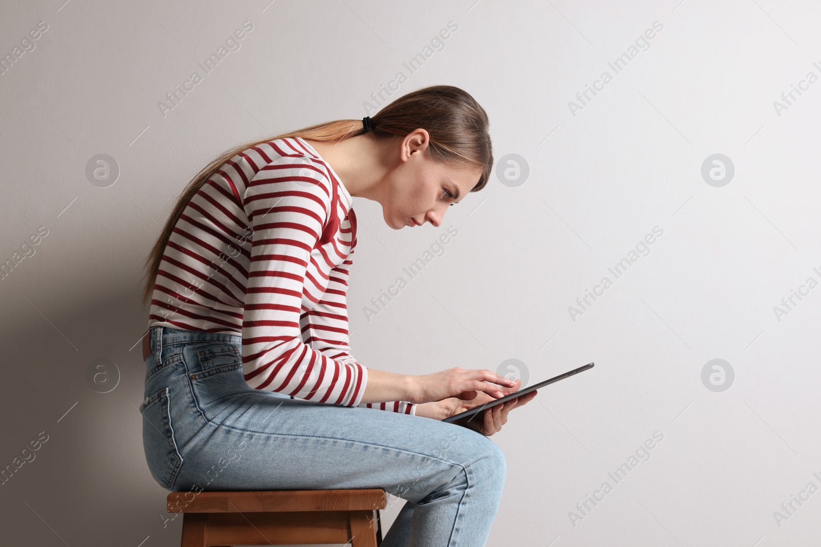 Photo of Woman with bad posture using tablet while sitting on stool against light grey background