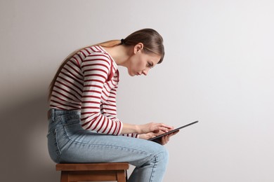 Woman with bad posture using tablet while sitting on stool against light grey background