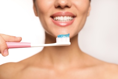 Photo of Woman holding toothbrush with paste on light background, closeup