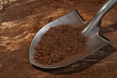 Photo of Metal shovel with fertile soil on dirty wooden surface