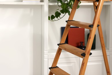 Photo of Wooden folding ladder near white shelving unit indoors